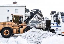 Effektiv snöplogning: en gul traktorgrävare lastar upp snö på en vit lastbils flak för bortforsling av snön.