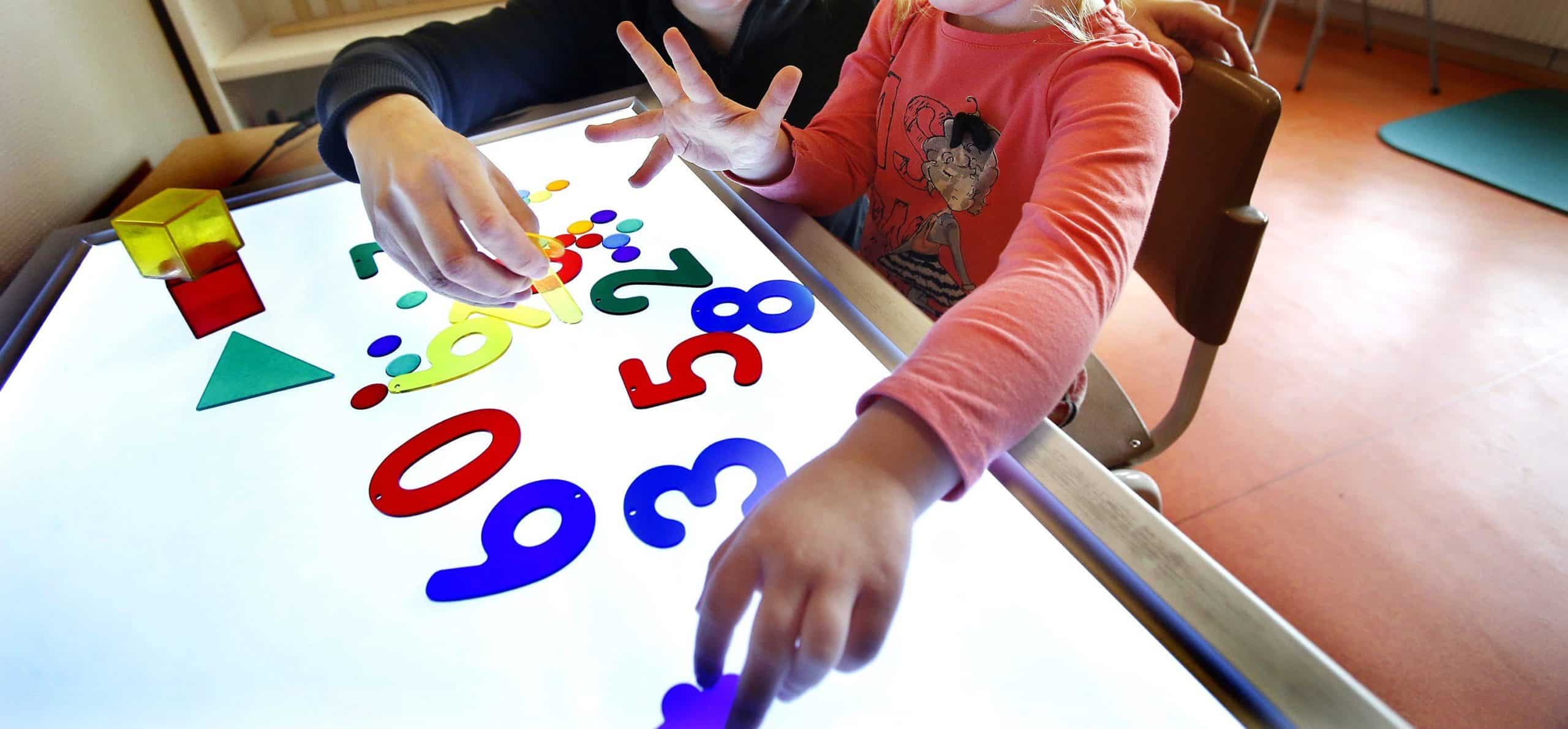 Förskolebarn leker med siffror i olika färger på ett ljusbord.