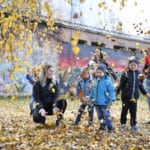 Barnfamilj leker vid Laxholmen. Alla är samlade under en björk och kastar gula höstlöv i luften.