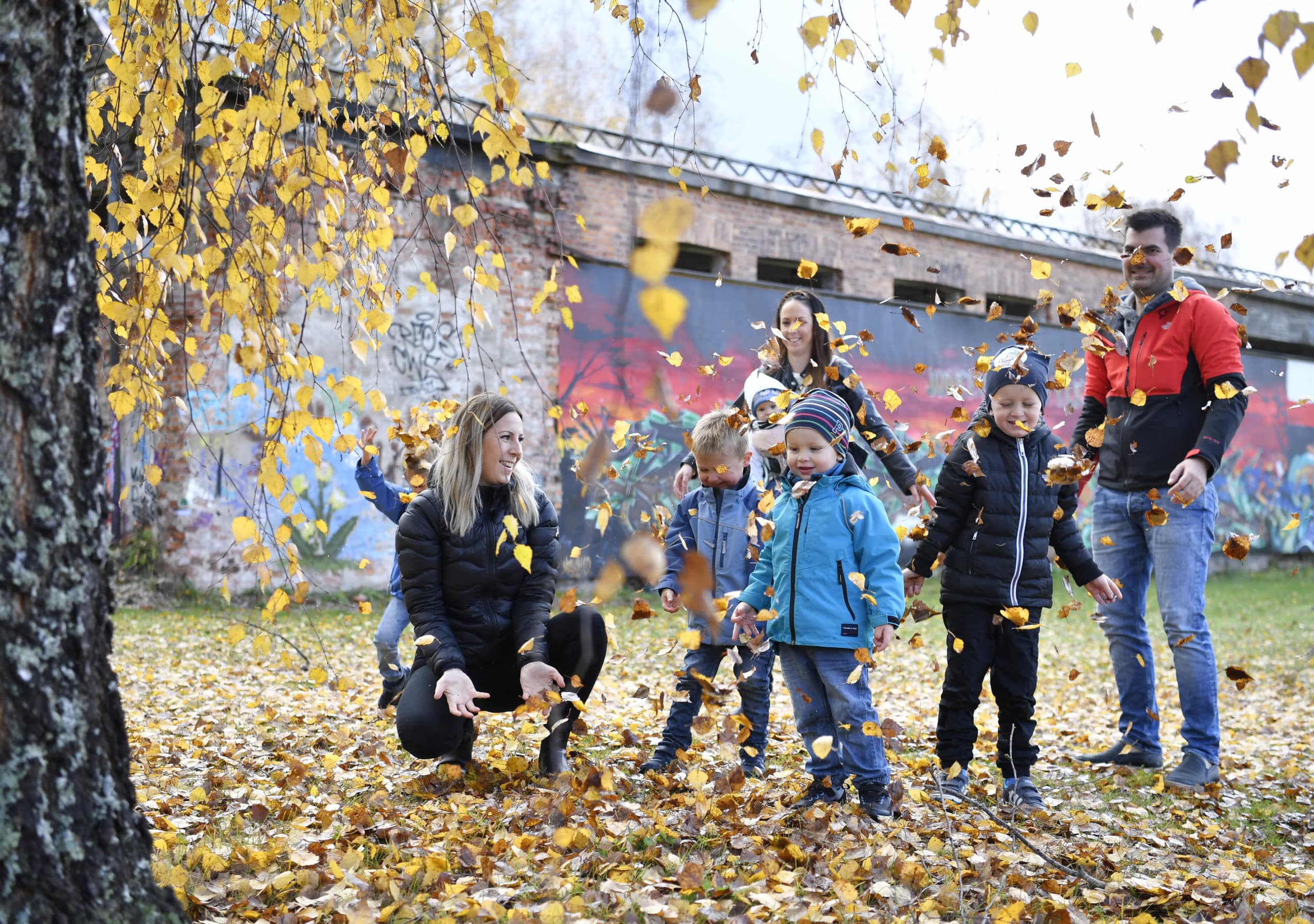 Barnfamilj leker vid Laxholmen. Alla är samlade under en björk och kastar gula höstlöv i luften.