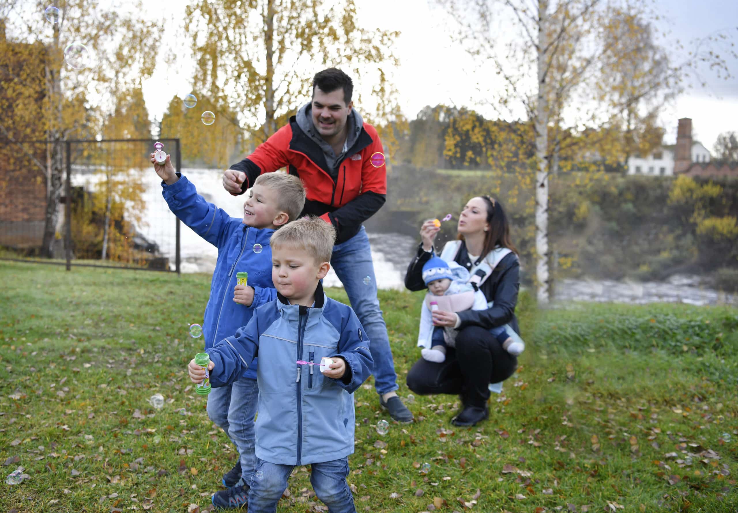 Mamma och pappa blåser såpbubblor tillsammans med sina tre barn vid Munkforsen.