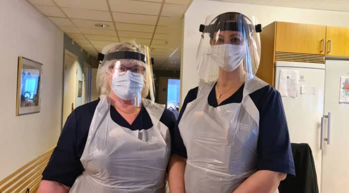 Sjuksköterskorna Lena Gillberg och Anna Torbrand stå bredvid varandra iklädda skyddsutrustning i form av visir, plastförkläde och munskydd 