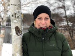 Leende kvinna står och lutar sig mot en björk.