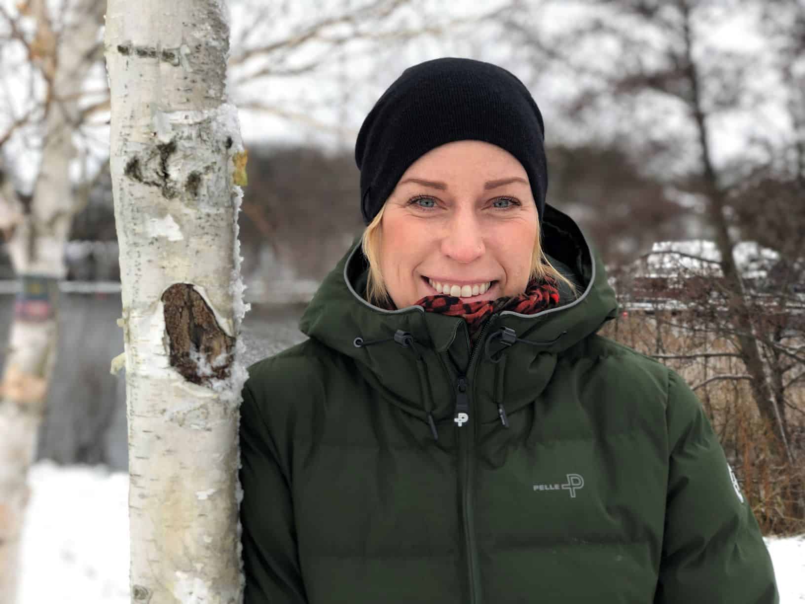 Leende kvinna står och lutar sig mot en björk.