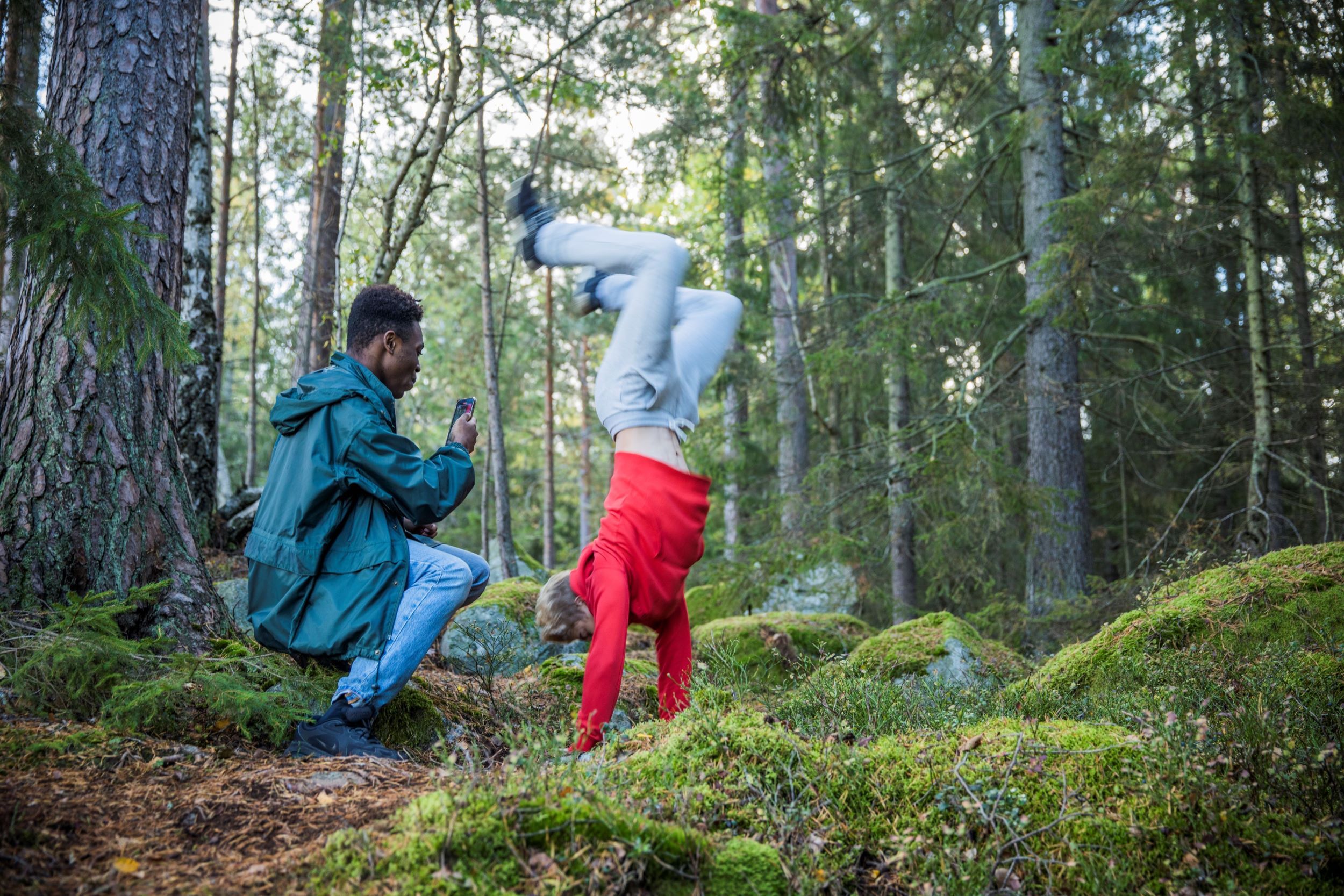 Kille fotograferar sin kompis som gör parcour i skogen.