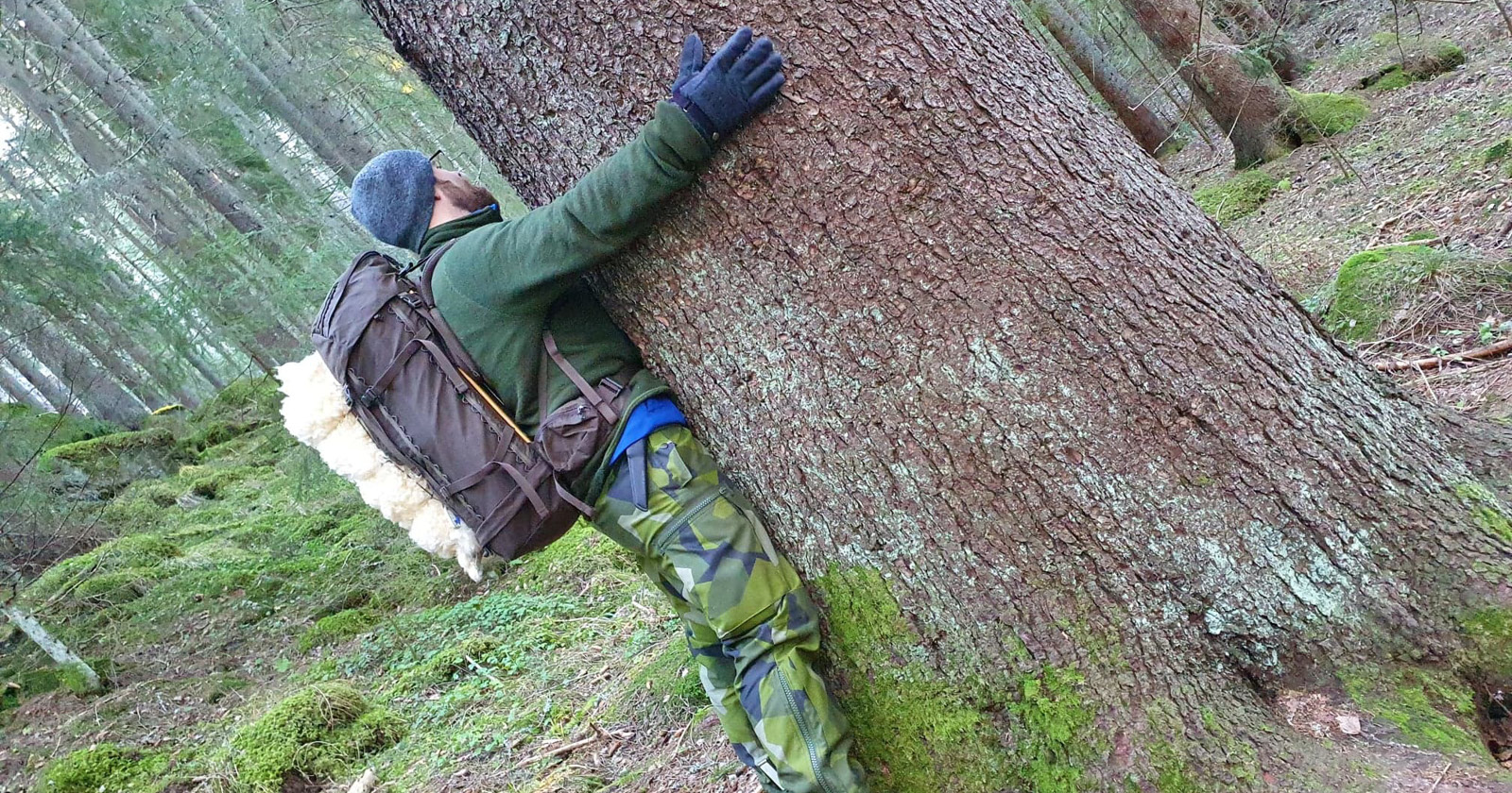 Eric står i skogen och kramar ett träd.