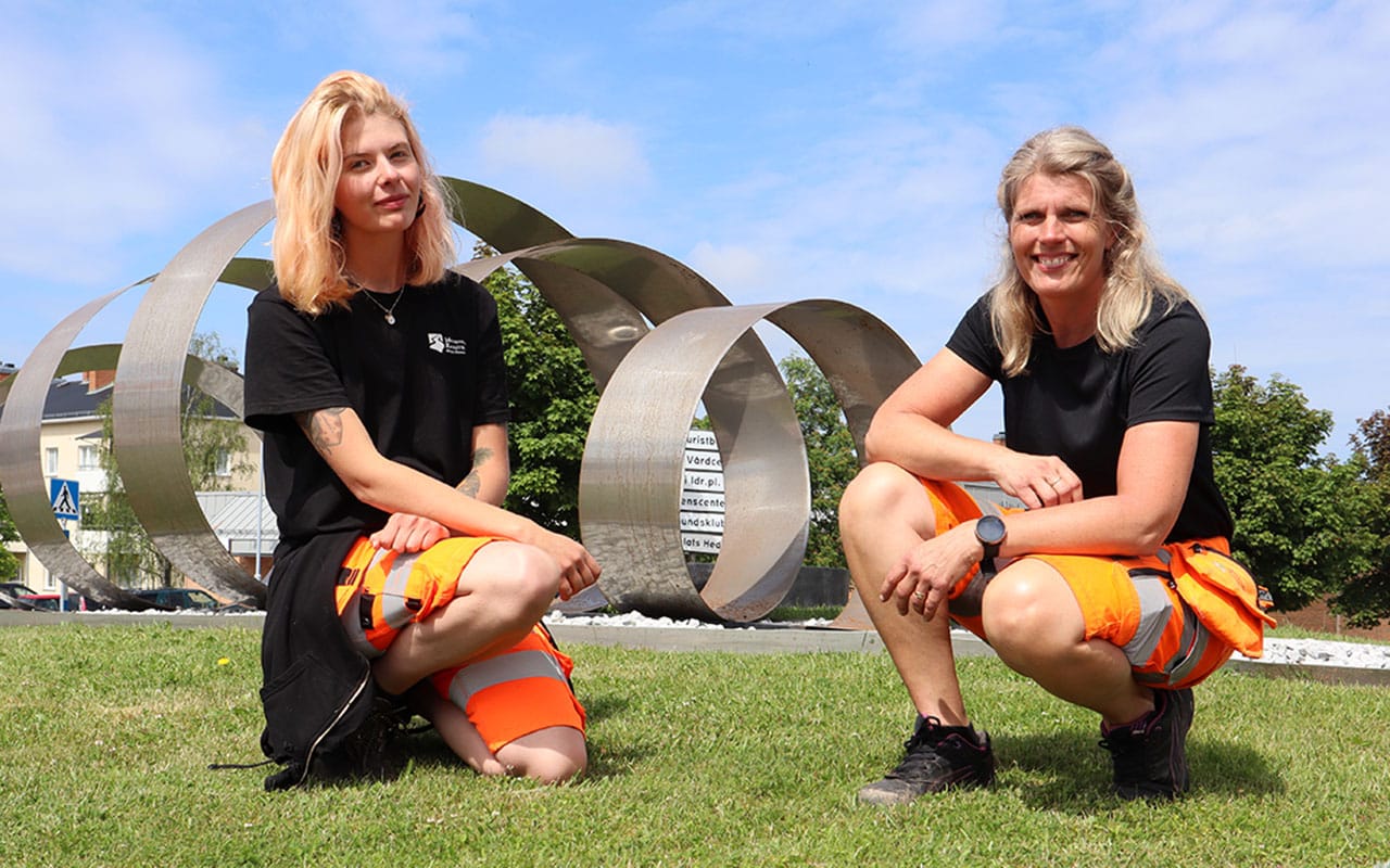 Megan och Ylva sitter på huk framför skulpturen Galax i rondellen .