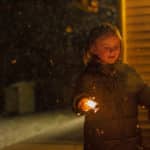 Liten flicka som står utomhus med två sprakande tomtebloss.