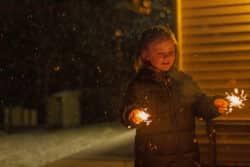 Liten flicka som står utomhus med två sprakande tomtebloss.