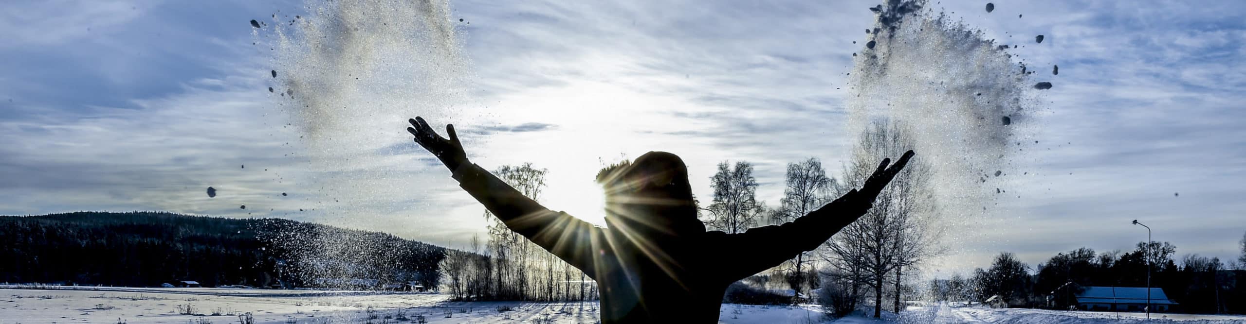 Person i täckjacka som slänger snö över huvudet.