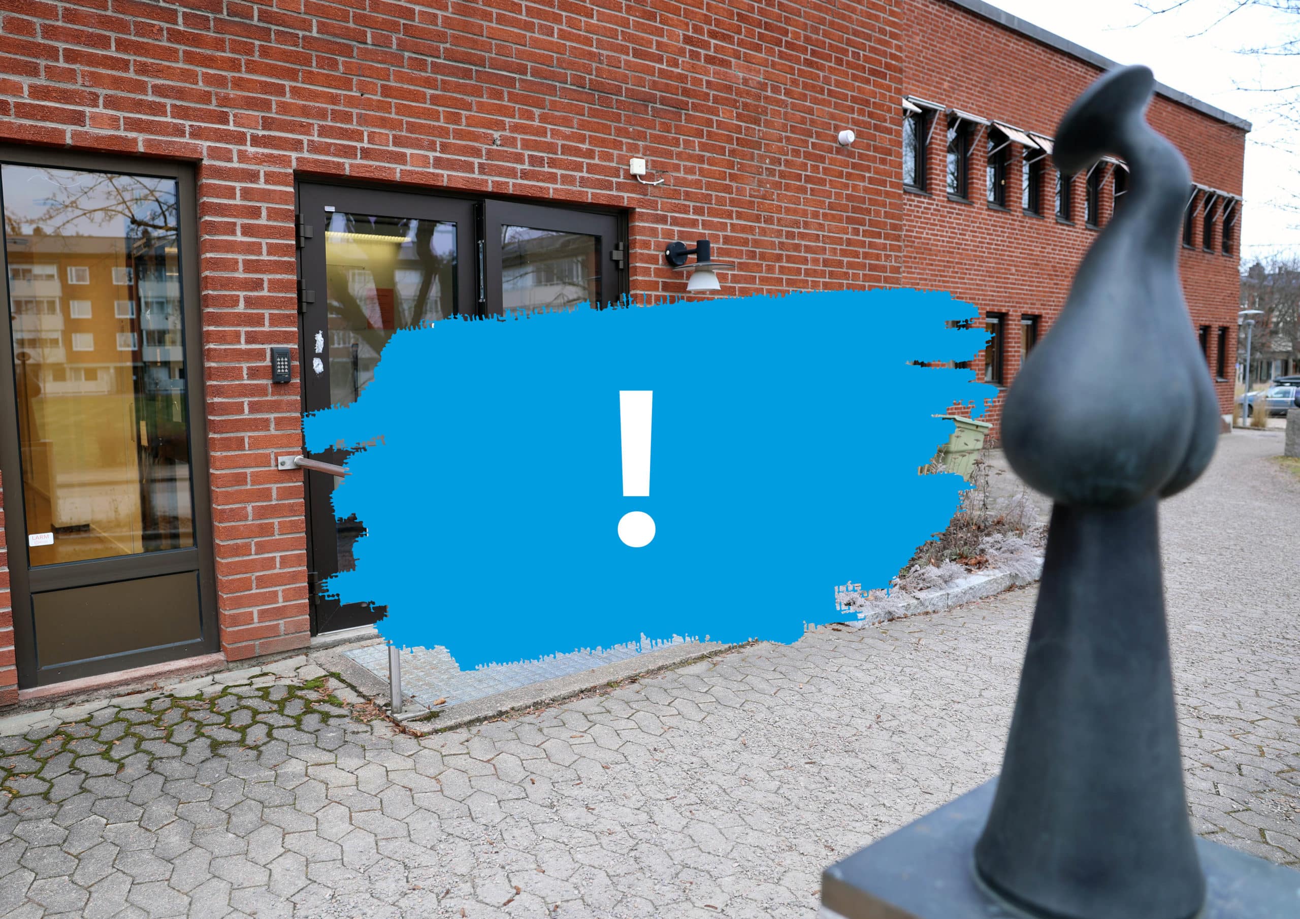 Blå målarfärg med ett utropstecken framför bild på entré till gamla Arbetsförmedlingen.