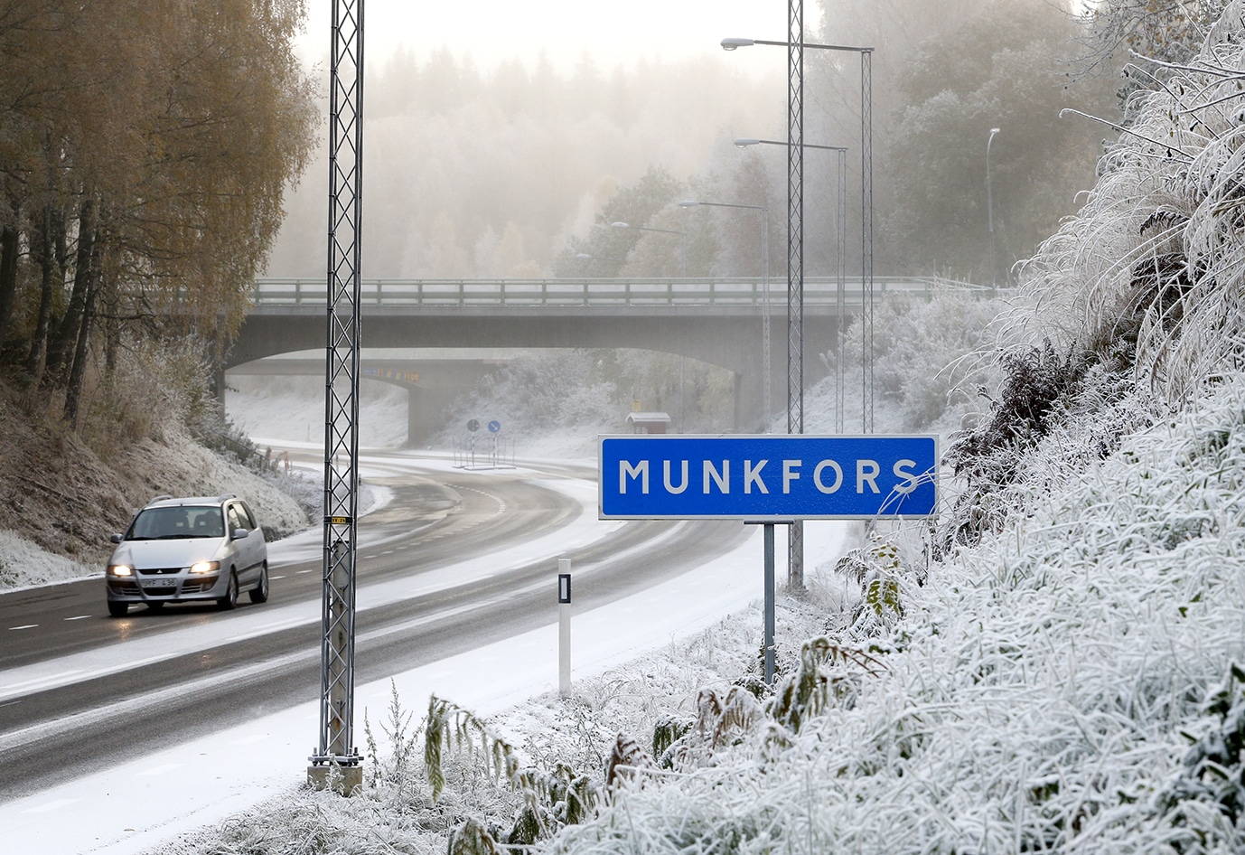 Bil kör på vinterväg intill Munkforsskylt