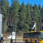 Två personer står vid en busshållsplats. En buss står parkerad med texten Sunne.