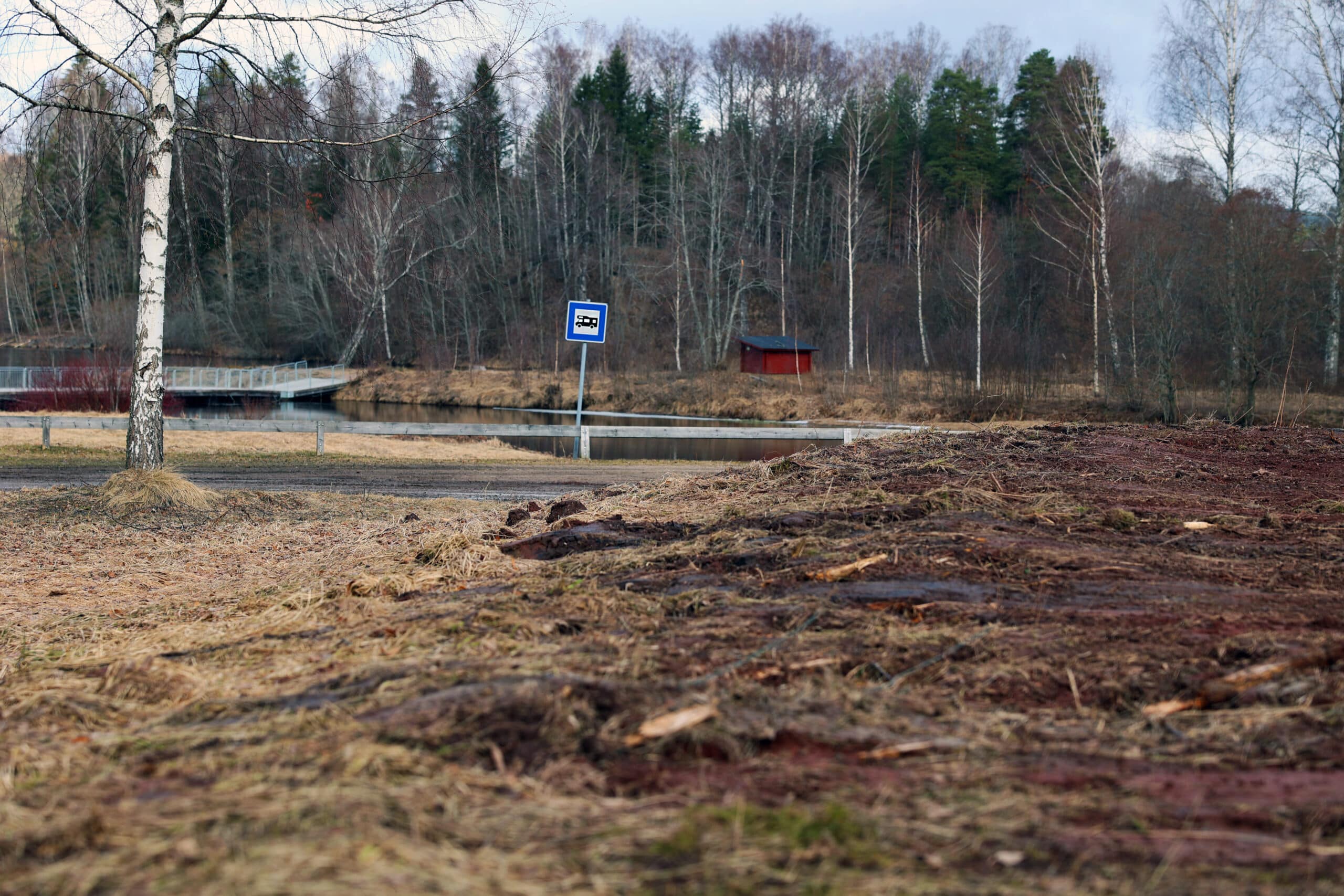 Jord i förgrunden. Ställplatsskylt i bakgrunden.